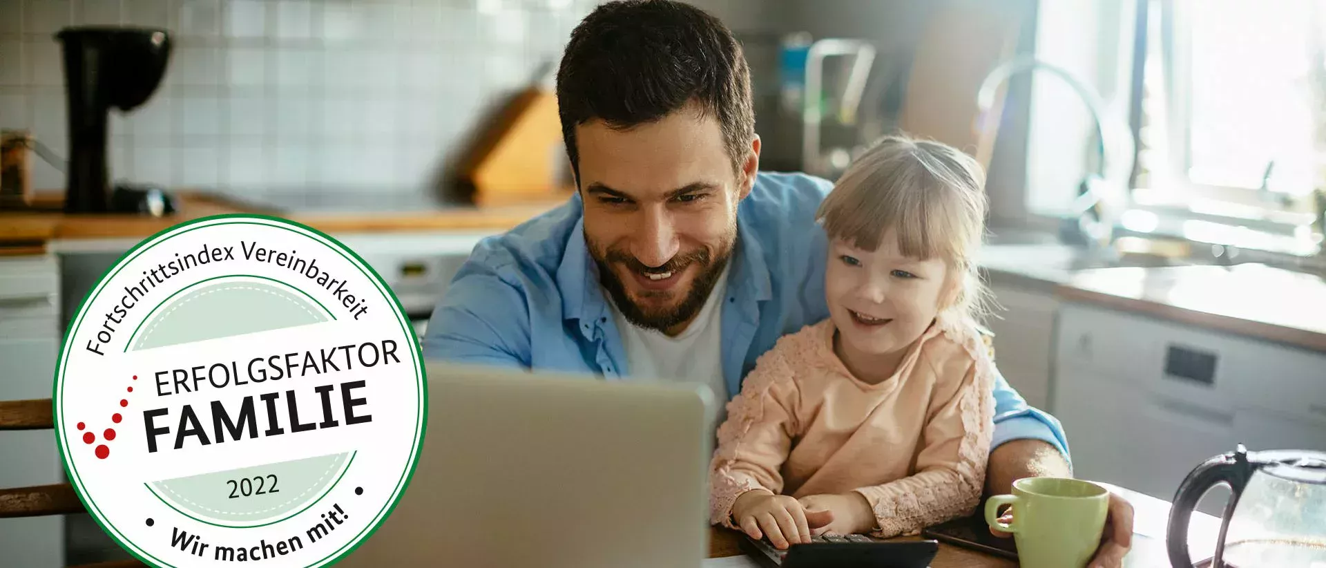 El padre se sienta a la mesa de la cocina con su hija pequeña y miran felices el portátil que tienen delante.